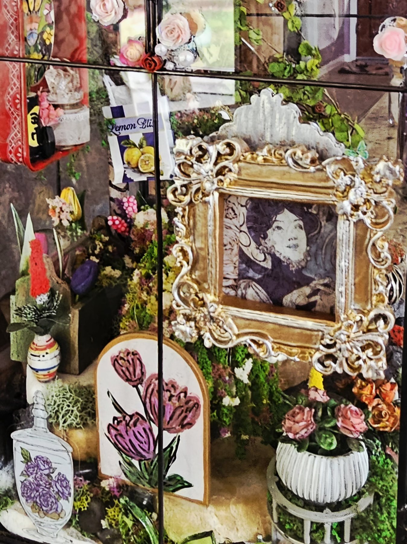 A richly detailed miniature room scene with a tiny gilded portrait frame, botanical prints and hand-built flowers